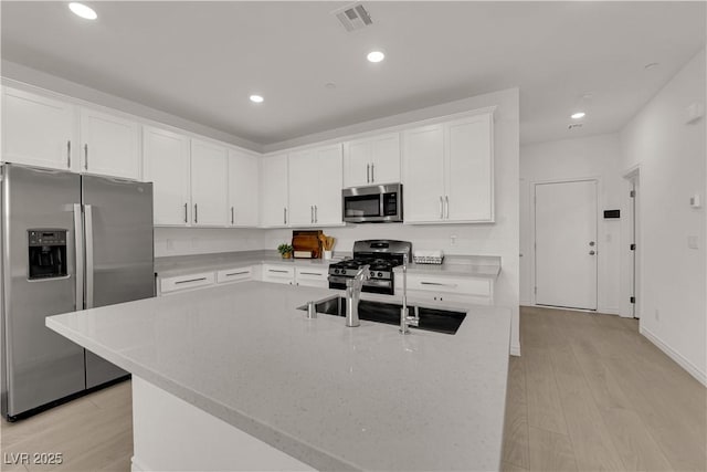 kitchen with appliances with stainless steel finishes, light wood-style flooring, white cabinets, recessed lighting, and a center island with sink