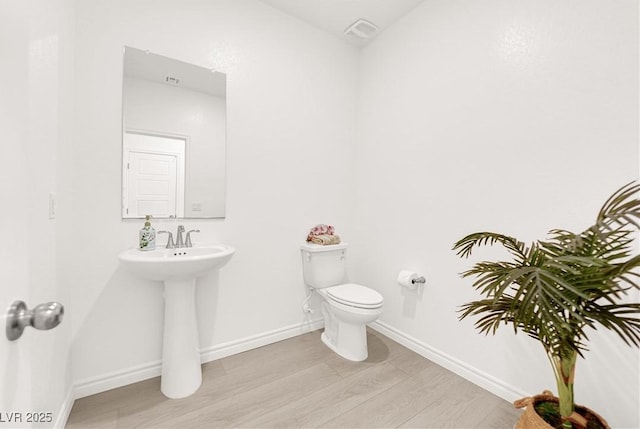 half bath with wood finished floors, toilet, and baseboards