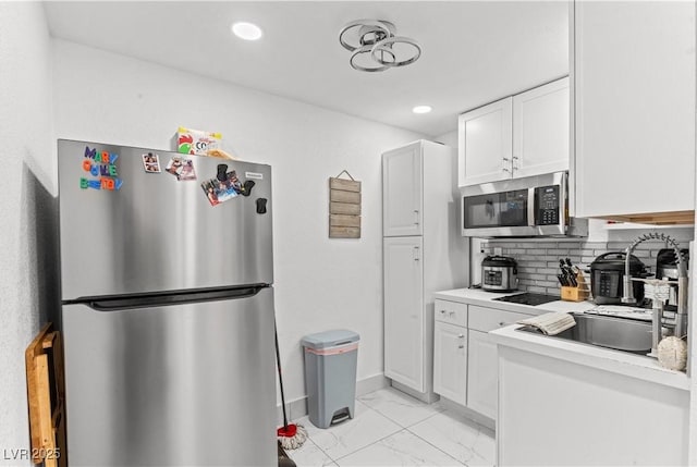 kitchen with appliances with stainless steel finishes, white cabinetry, light marble finish floors, light countertops, and backsplash
