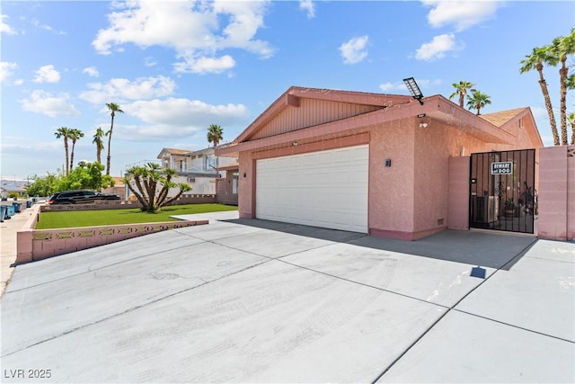 view of property exterior with an attached garage, driveway, a gate, stucco siding, and a yard