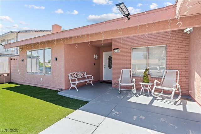 rear view of property with brick siding, a patio area, stucco siding, and a lawn