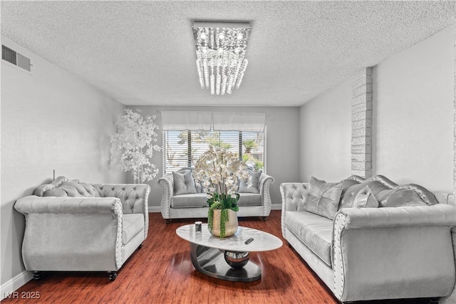 living area with a textured ceiling, a chandelier, wood finished floors, and baseboards