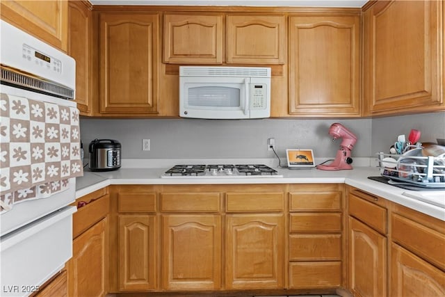 kitchen with white appliances, a warming drawer, light countertops, and brown cabinets