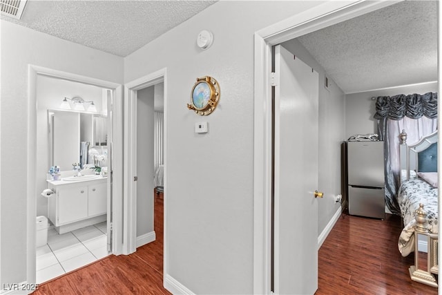 hallway with a textured ceiling, wood finished floors, baseboards, and a sink