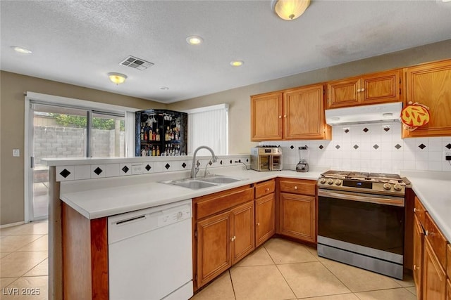 kitchen with white dishwasher, stainless steel gas range, under cabinet range hood, a sink, and a peninsula