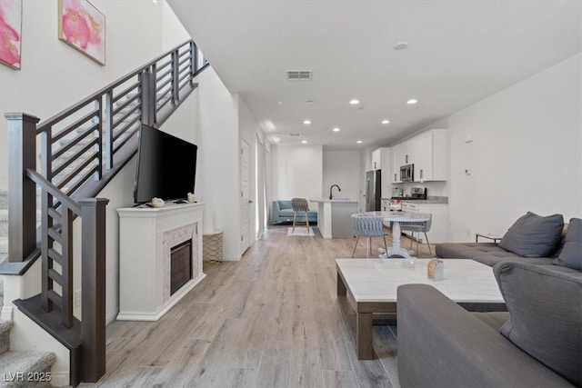 living area with light wood-style flooring, stairway, recessed lighting, and a glass covered fireplace