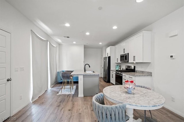 4526 Cloudrest Peak St, North Las Vegas, NV 89031 - kitchen featuring appliances with stainless steel finishes, a sink, an island with sink, light wood-type flooring, and white cabinets