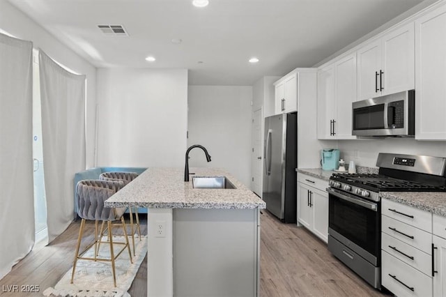 kitchen featuring stainless steel appliances, a sink, a center island with sink, light wood finished floors, and white cabinetry
