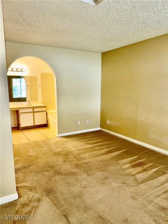 carpeted empty room with arched walkways, a textured ceiling, and baseboards