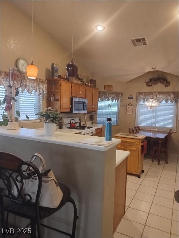 kitchen with stainless steel microwave, white gas range oven, vaulted ceiling, light tile patterned flooring, and light countertops