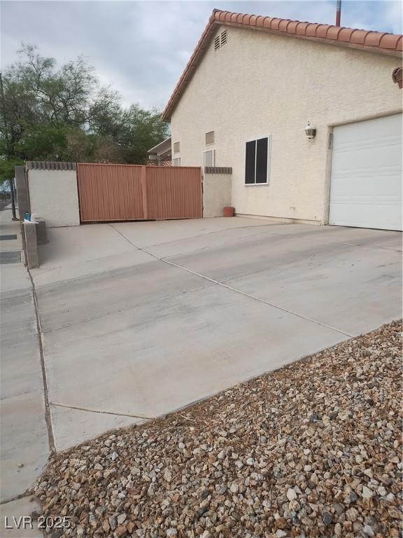 view of property exterior with an attached garage, driveway, fence, and stucco siding