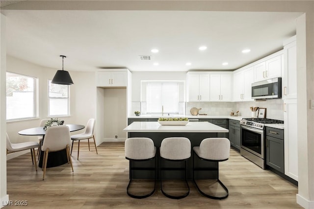 kitchen with appliances with stainless steel finishes, a kitchen island, backsplash, light countertops, and light wood finished floors
