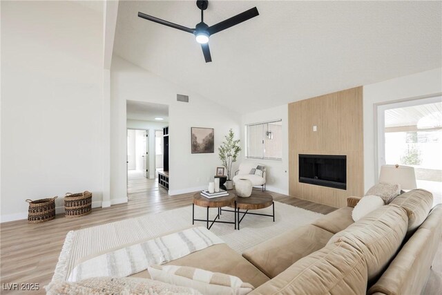 living room featuring ceiling fan, light wood-style flooring, a large fireplace, baseboards, and high vaulted ceiling
