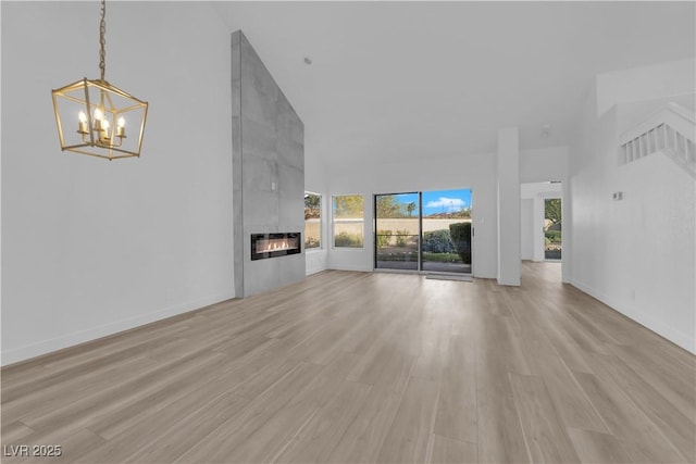 6940 Emerald Springs Ln, Las Vegas, NV 89113 - unfurnished living room with a towering ceiling, a chandelier, light wood-style floors, a fireplace, and baseboards