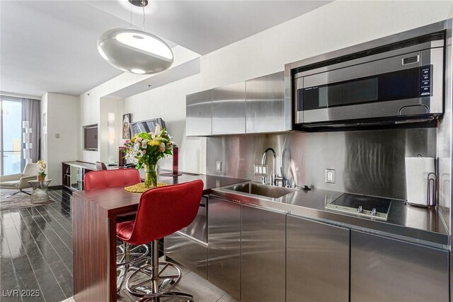 kitchen featuring stainless steel microwave, stainless steel countertops, modern cabinets, black electric stovetop, and a sink