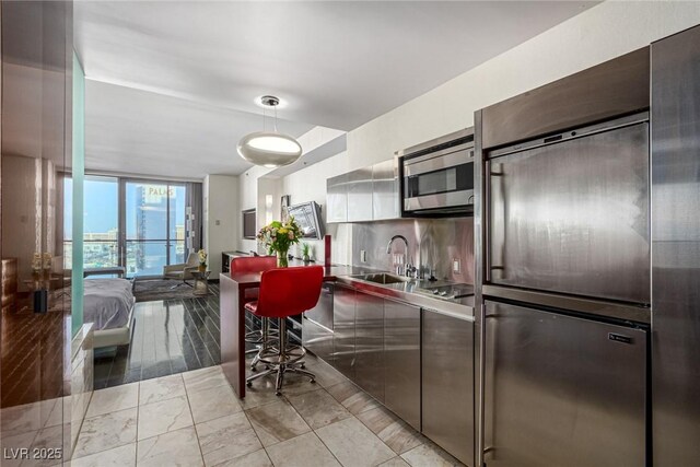 kitchen featuring stainless steel microwave, a sink, built in refrigerator, modern cabinets, and a wall of windows