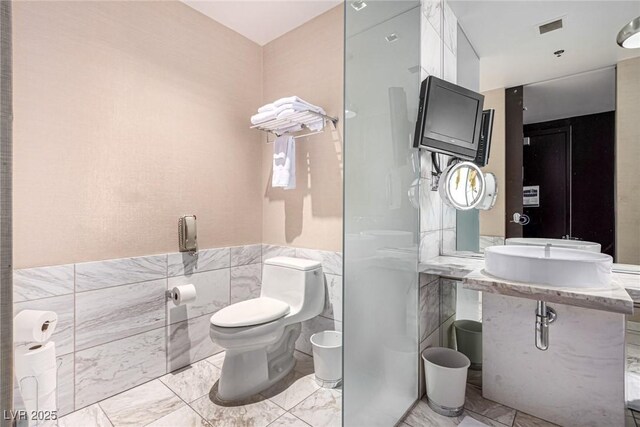 bathroom featuring tile walls, marble look tiles, toilet, a bidet, and wainscoting