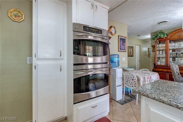 604 N Torrey Pines Dr, Las Vegas, NV 89107 - kitchen with stainless steel double oven, white cabinetry, light tile patterned flooring, a textured ceiling, and light stone countertops