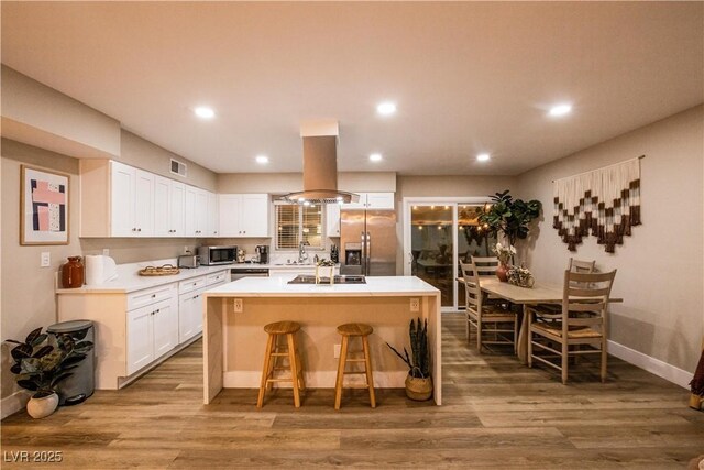 2043 Sombrero Dr, Las Vegas, NV 89169 - kitchen featuring appliances with stainless steel finishes, island range hood, white cabinetry, a kitchen bar, and wood finished floors