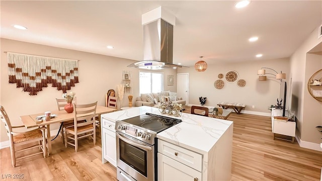 2043 Sombrero Dr, Las Vegas, NV 89169 - kitchen featuring stainless steel range with electric cooktop, open floor plan, island range hood, white cabinets, and light wood-type flooring