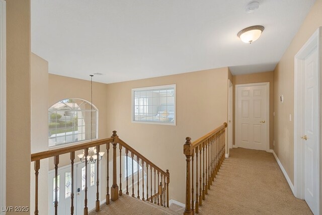 hall featuring an upstairs landing, light colored carpet, a chandelier, and baseboards