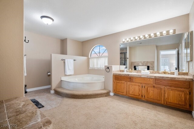 bathroom featuring a bath, a fireplace, a walk in shower, double vanity, and baseboards