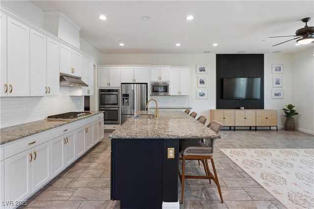 kitchen featuring appliances with stainless steel finishes, backsplash, white cabinets, under cabinet range hood, and recessed lighting