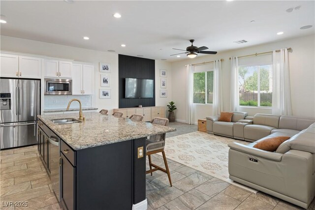 kitchen with appliances with stainless steel finishes, a sink, open floor plan, a breakfast bar area, and white cabinets