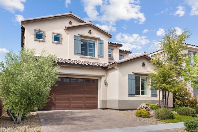 mediterranean / spanish home with stucco siding, a garage, a tile roof, and decorative driveway