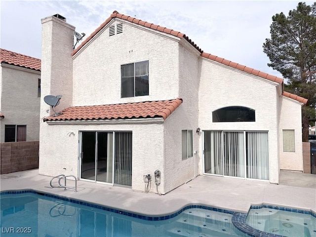 rear view of house with a tile roof, stucco siding, a patio area, and a pool with connected hot tub
