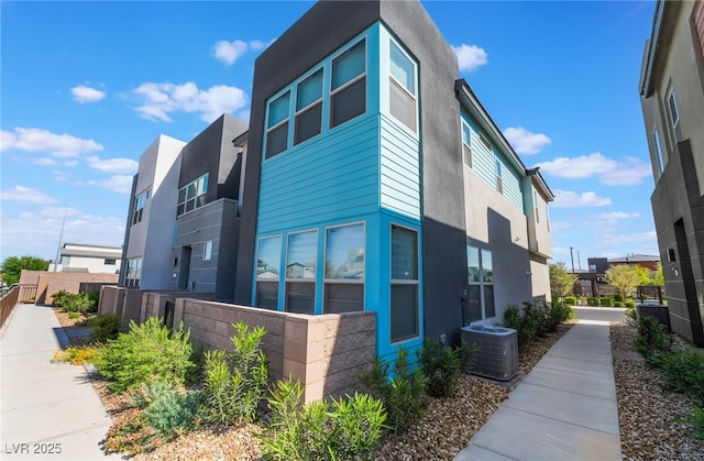 view of side of property featuring central air condition unit, fence, and stucco siding