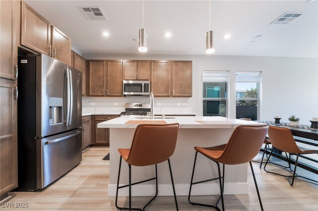 kitchen featuring appliances with stainless steel finishes, a sink, light countertops, a breakfast bar, and a kitchen island with sink