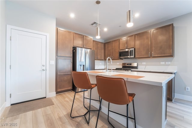 kitchen with appliances with stainless steel finishes, baseboards, light countertops, a kitchen breakfast bar, and light wood-type flooring