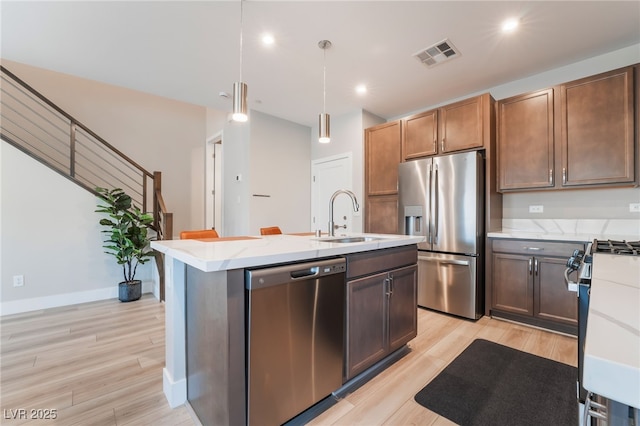 kitchen featuring appliances with stainless steel finishes, a sink, light wood-style floors, an island with sink, and recessed lighting