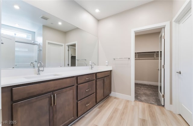 full bathroom featuring a stall shower, wood finished floors, double vanity, a spacious closet, and recessed lighting