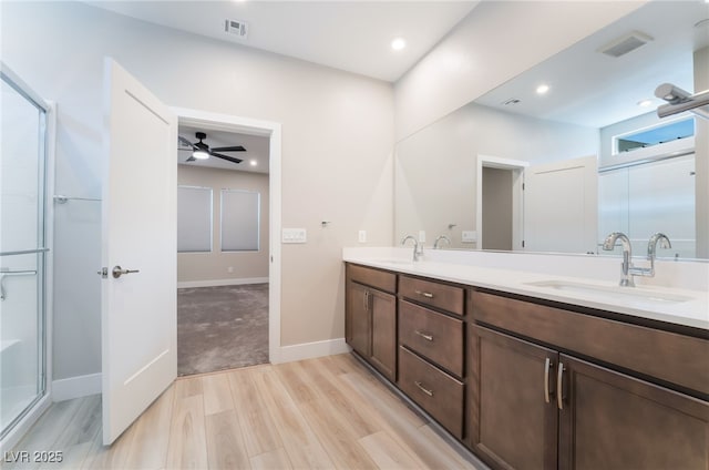 bathroom featuring wood finished floors, a shower with door, ceiling fan, double vanity, and baseboards