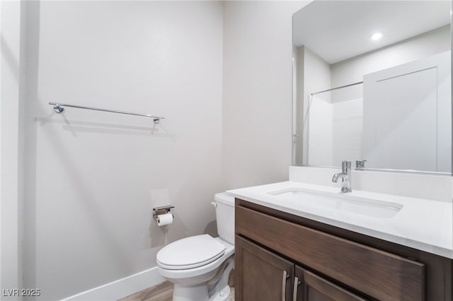 bathroom with toilet, vanity, baseboards, a shower, and wood finished floors