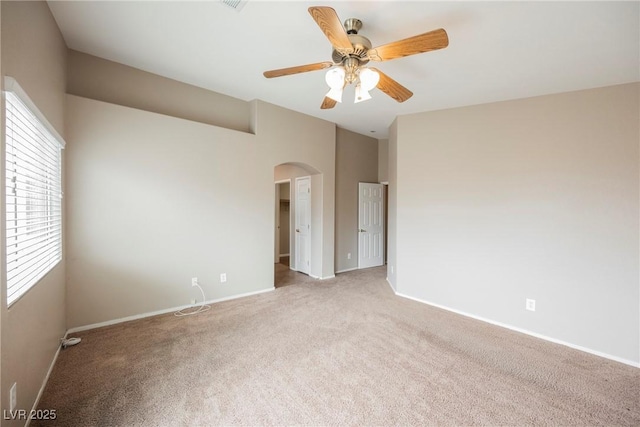 empty room with arched walkways, light carpet, baseboards, and ceiling fan