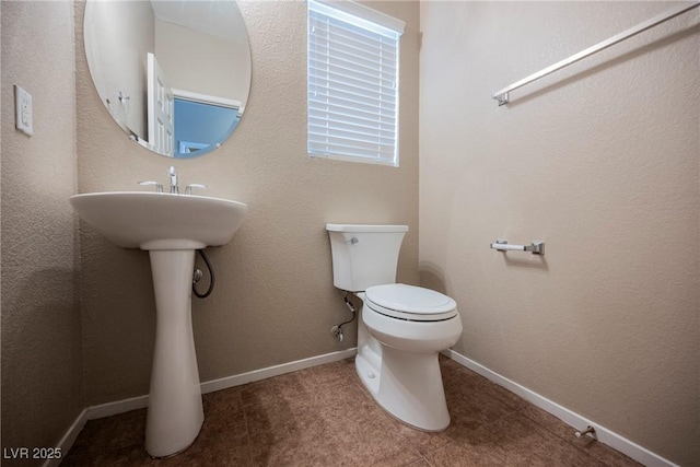 half bath featuring toilet, baseboards, and a sink