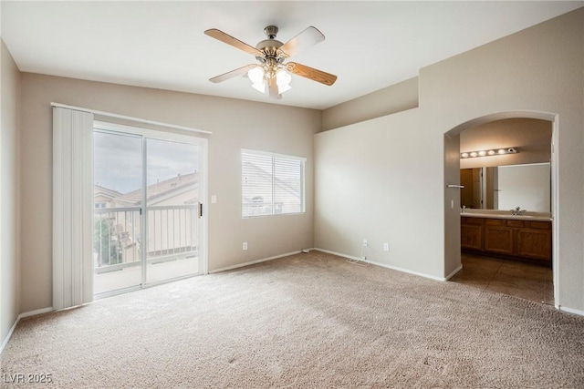 unfurnished room with carpet, arched walkways, ceiling fan, a sink, and baseboards