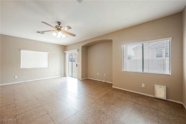empty room with ceiling fan, healthy amount of natural light, baseboards, and arched walkways