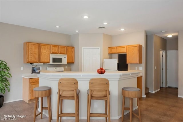kitchen with white microwave, refrigerator, light countertops, a kitchen breakfast bar, and recessed lighting