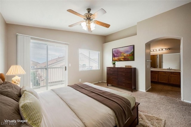 carpeted bedroom featuring arched walkways, access to outside, a sink, ensuite bath, and baseboards