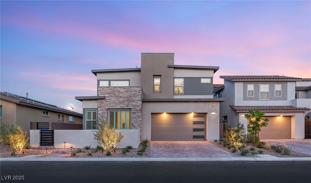 view of front of property with stucco siding, stone siding, an attached garage, and driveway