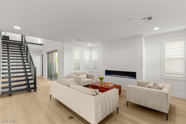 living area featuring light wood finished floors, a lit fireplace, stairway, recessed lighting, and baseboards