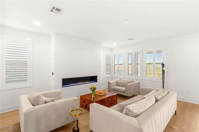 living room featuring a glass covered fireplace, light wood-style floors, recessed lighting, and baseboards