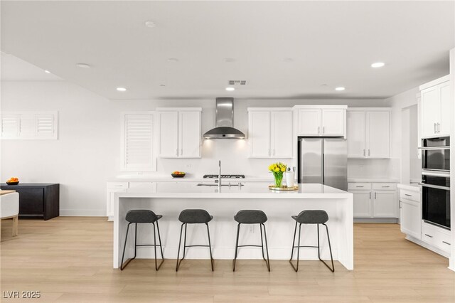 kitchen with freestanding refrigerator, wall chimney range hood, recessed lighting, a kitchen bar, and white cabinetry