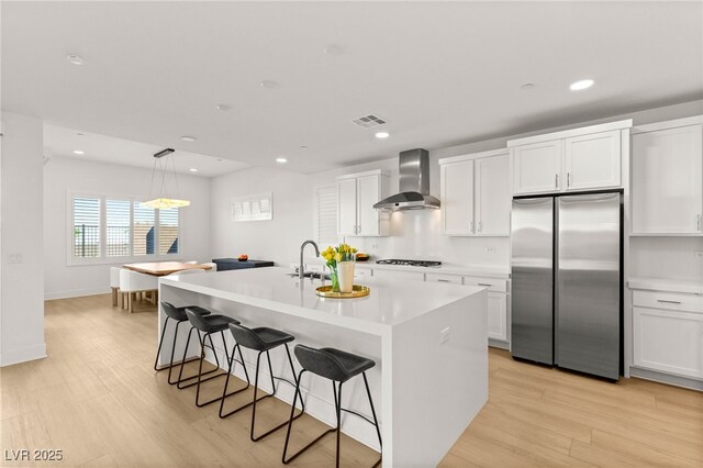 kitchen featuring freestanding refrigerator, wall chimney range hood, a breakfast bar area, a kitchen island with sink, and recessed lighting