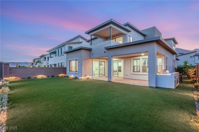 back of house at dusk featuring stucco siding, a balcony, and a patio area