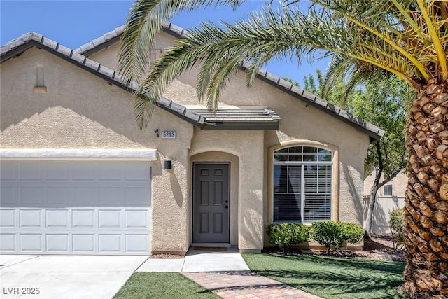 view of front of house with stucco siding, a garage, a tile roof, and concrete driveway
